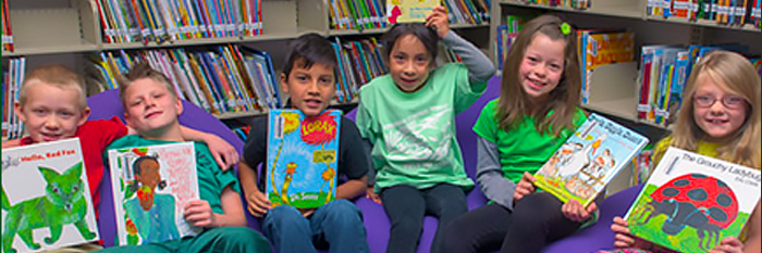 Five school aged children sitting on purple cushion chairs at the library smiling and holding books